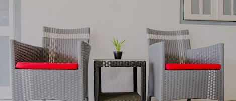 Two wicker chairs with red cushions, a small table with a plant, and a window with frosted glass panes.
