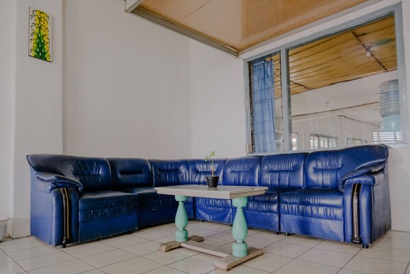 A blue leather sofa with a small table in front, a potted plant, and a window with curtains.