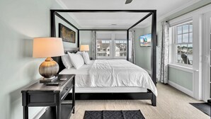 A modern bedroom with a four-poster bed, a ceiling fan, and a view of the city through large windows.
