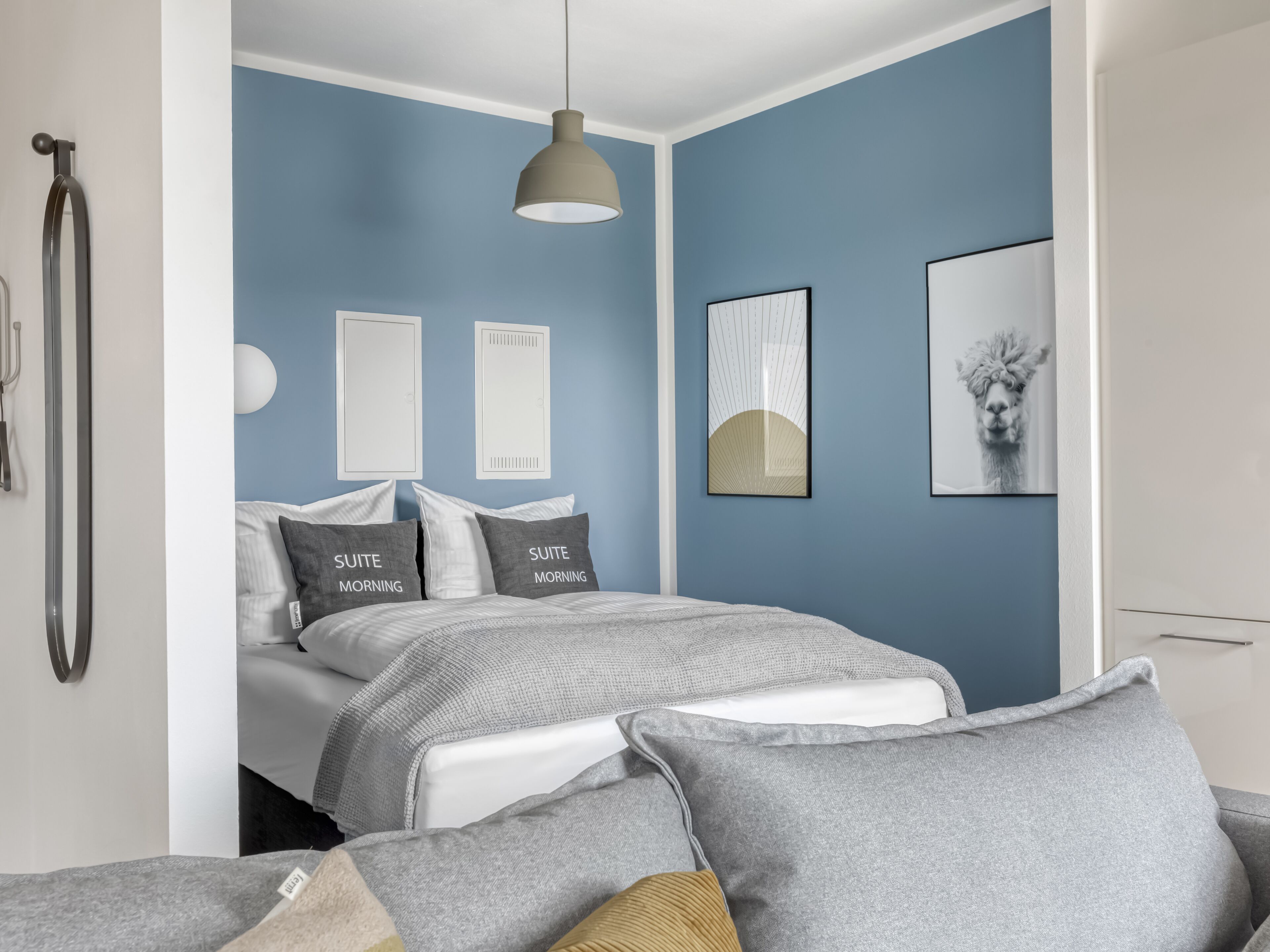 A modern bedroom with a bed, grey bedding, and a blue accent wall.