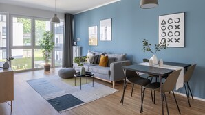 Un salon moderne avec un canapé gris, une table à manger avec des chaises, une table basse et une grande fenêtre avec des rideaux.
