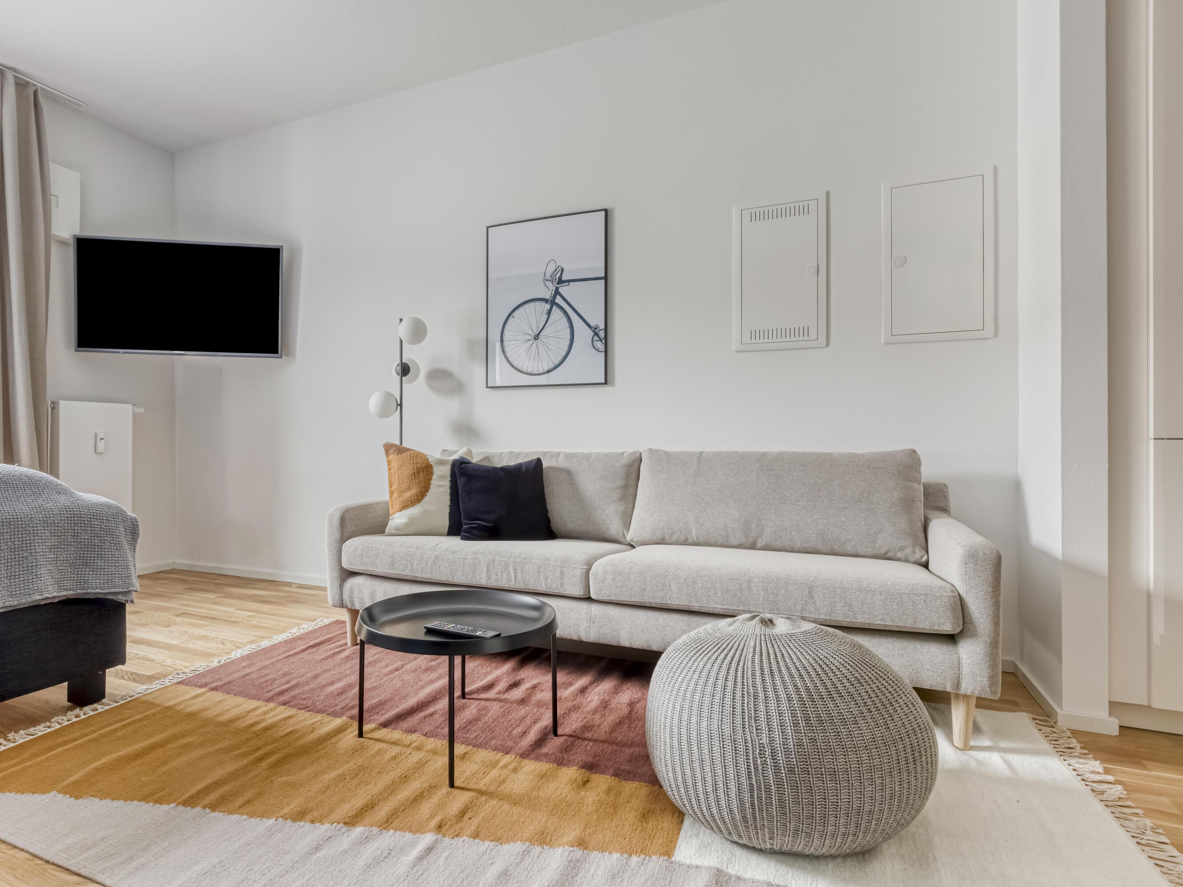Un salon moderne comprenant un canapé, une table basse, un pouf rond et un téléviseur fixé au mur.