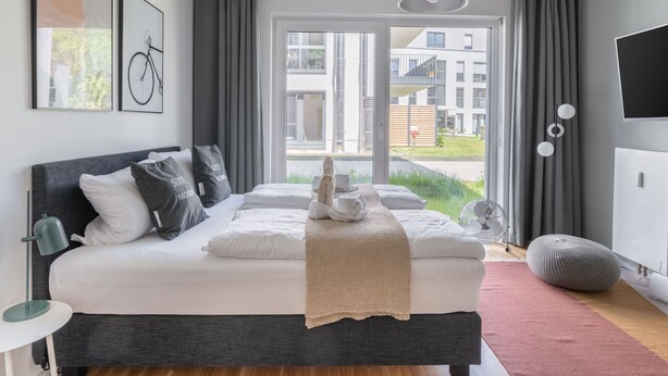 Une chambre moderne avec un grand lit, une table de chevet, une lampe, un ventilateur et un téléviseur.