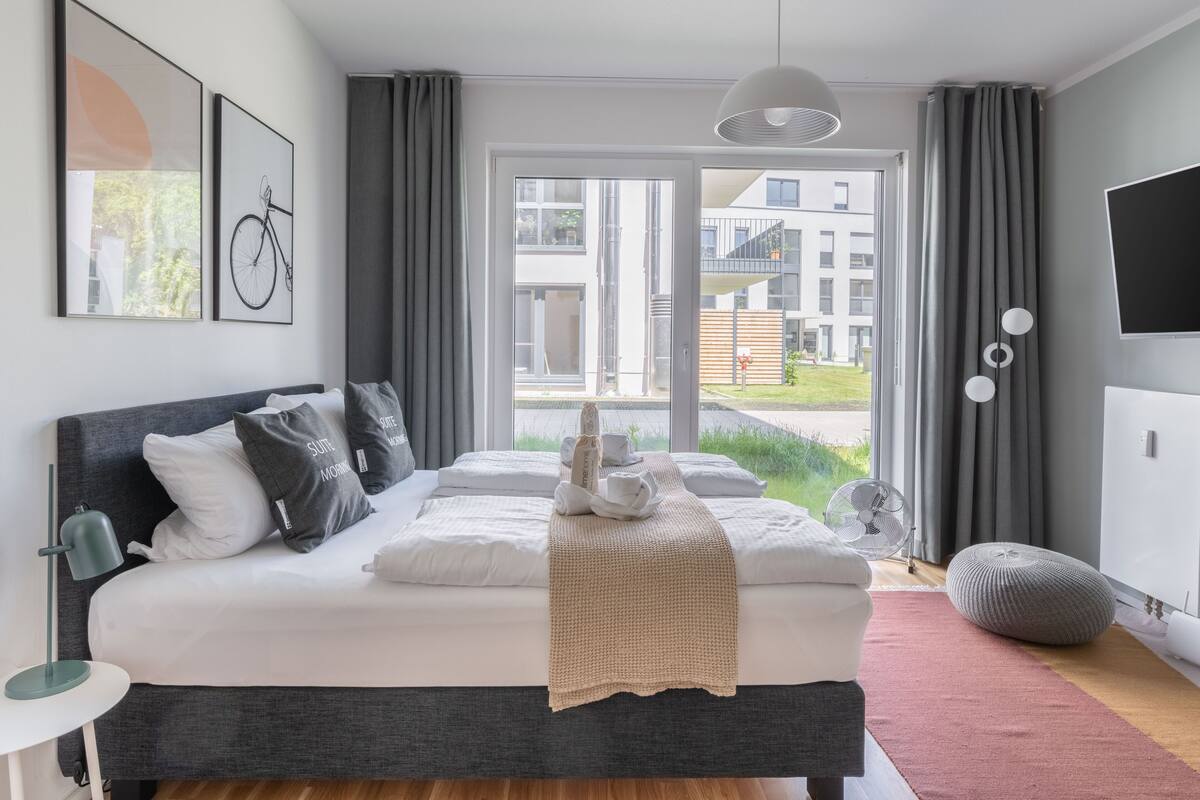 Een moderne slaapkamer met een groot bed, nachtkastje, lamp, ventilator en televisie.
