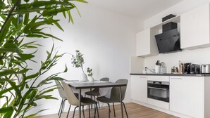 Une cuisine moderne avec des meubles blancs, un plan de travail noir et un four encastré. On y trouve une table à manger avec des chaises et une plante en pot.