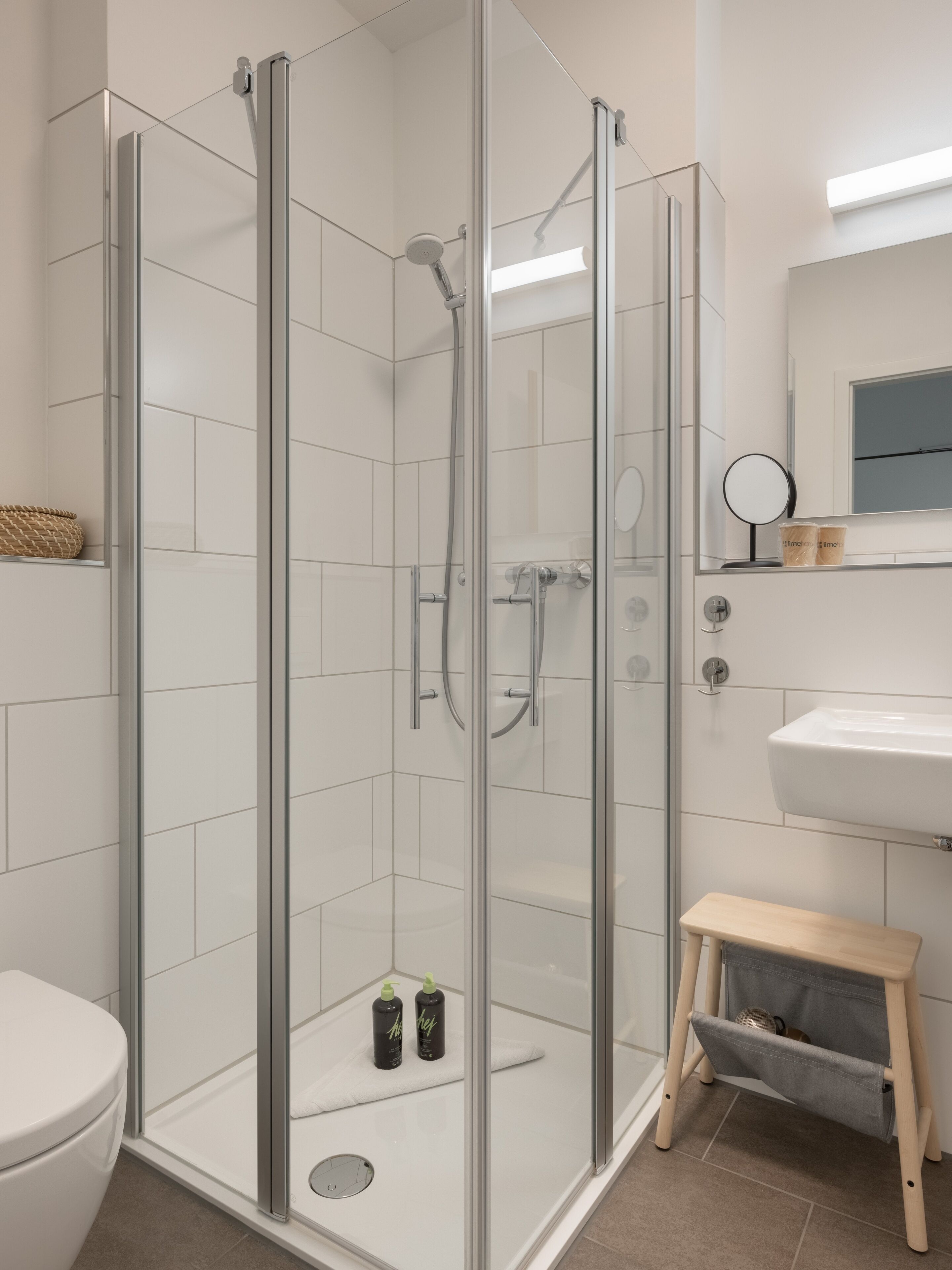 A modern bathroom with a glass-enclosed shower, a white sink, and a small wooden stool.