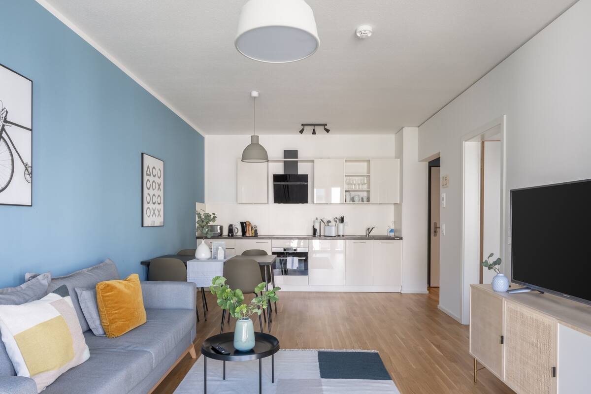 Een moderne woonkamer met een grijze bank, een salontafel en een tv op een houten kast.