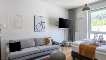 Ett modernt hotellrum med en soffa, en säng, en tv och ett fönster med utsikt över grönområden.