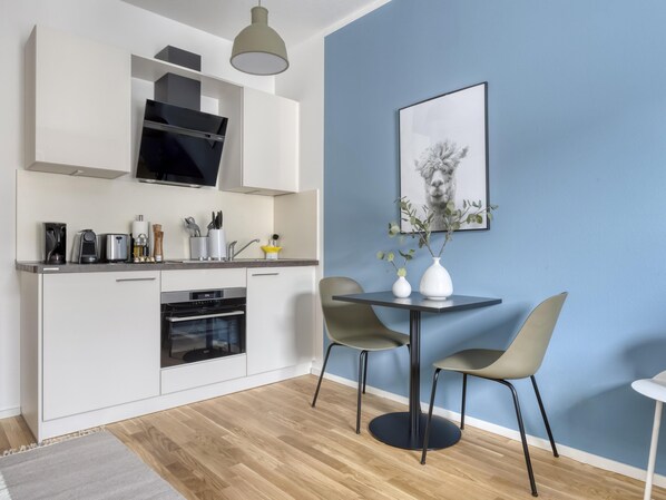 A modern kitchen with white cabinets, a built-in oven, and a dining area with two chairs and a table.