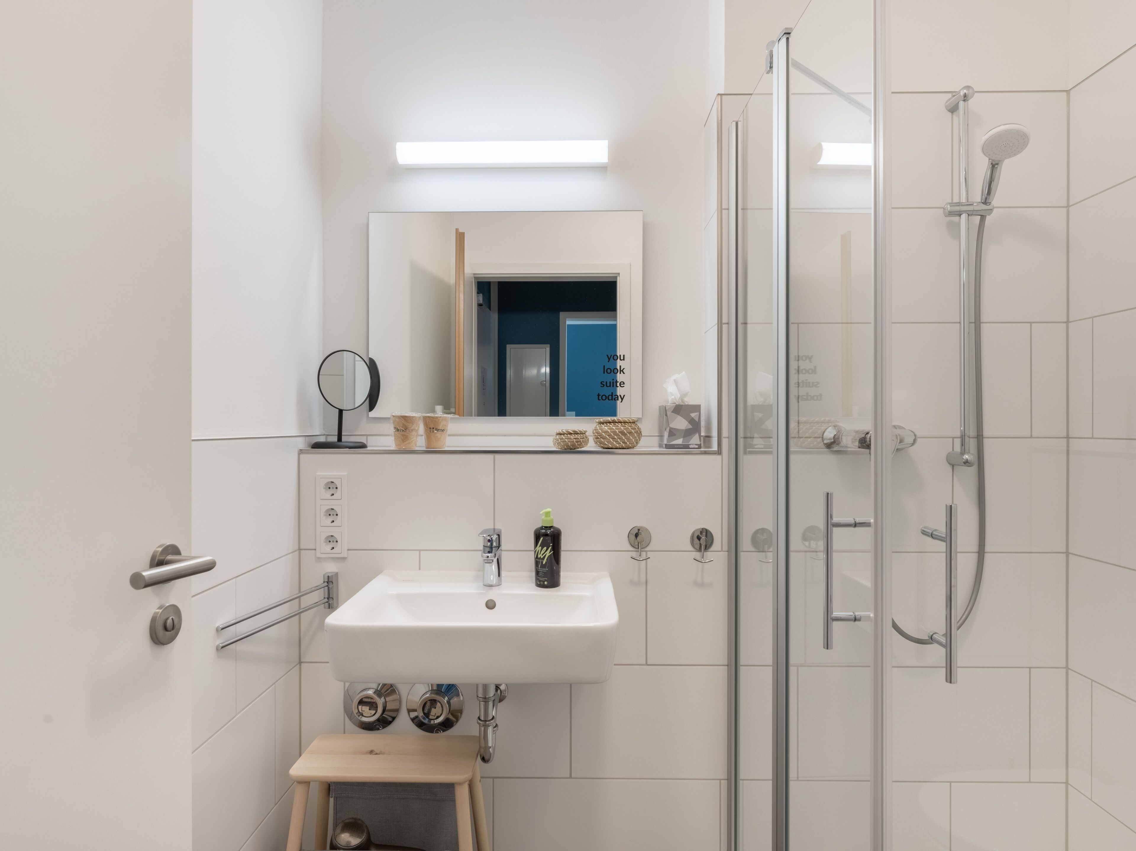 Une salle de bain moderne avec une douche à parois de verre, un lavabo blanc et un petit tabouret.