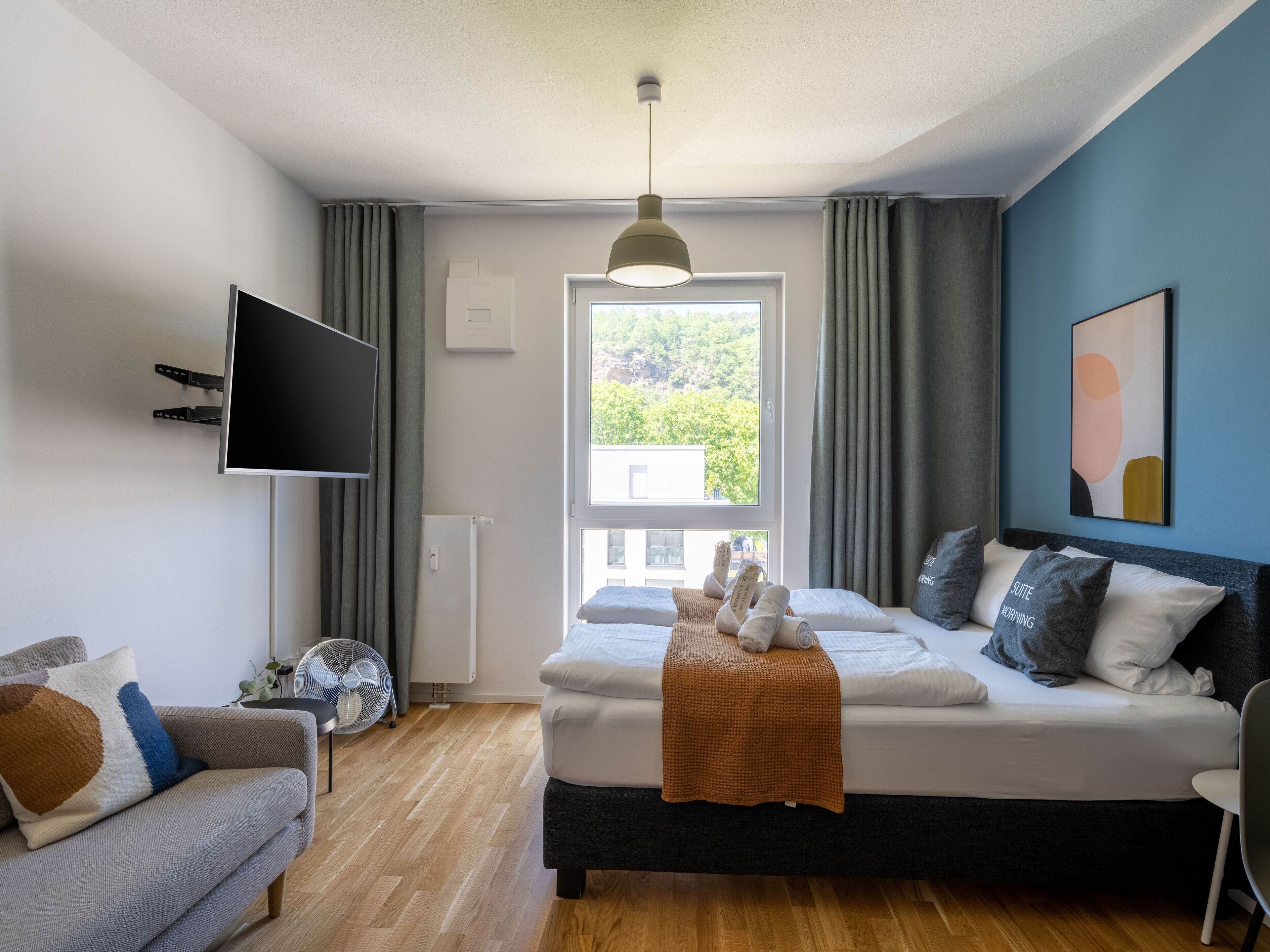 A modern bedroom with a bed, a sofa, a TV, and a window with curtains.