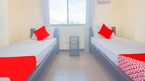 Une chambre d’hôtel avec deux lits simples, une fenêtre avec des rideaux, une petite table et un appareil de climatisation.