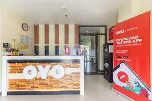 Uma mesa de recepção com o logotipo 'OYO', um relógio e diversos avisos na parede.