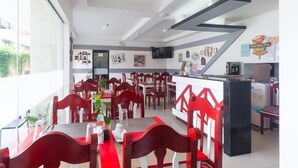 Un restaurant moderne avec des chaises et des tables rouges, un espace cuisine et une grande fenêtre laissant entrer la lumière naturelle.