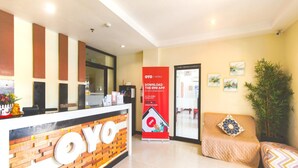 Un espace d’accueil d’hôtel comprenant un comptoir de réception, un canapé agrémenté de coussins à motifs et une grande enseigne OYO Hotels faisant la promotion d’une application mobile.