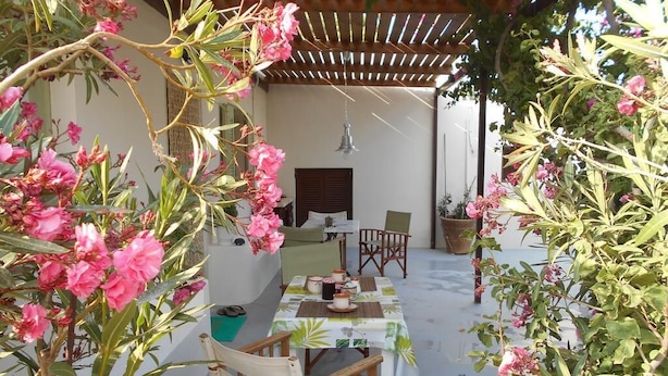 En uteplats med ett bord och stolar, omgiven av blommande växter och en pergola.