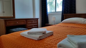 Una habitación de hotel con cama, mesita de noche, lámpara, armario y ventana con cortinas.