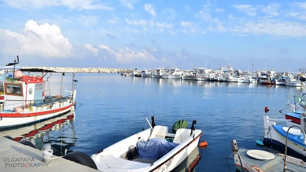 Un puerto deportivo con varios barcos amarrados, un muelle y una costa distante con edificios.