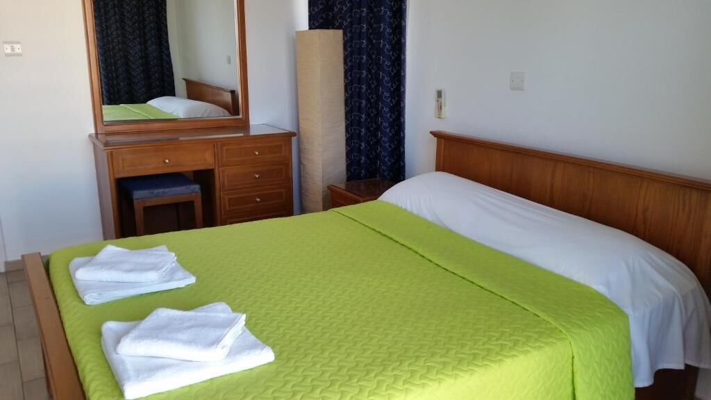 Una habitación de hotel con una cama, un aparador de madera, un espejo y una ventana con cortinas.