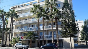 Un edificio de varios pisos con balcones, palmeras y coches estacionados.