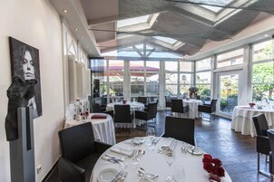 Un restaurante con mesas redondas dispuestas para comer, ventanas amplias y un techo alto con tragaluces.