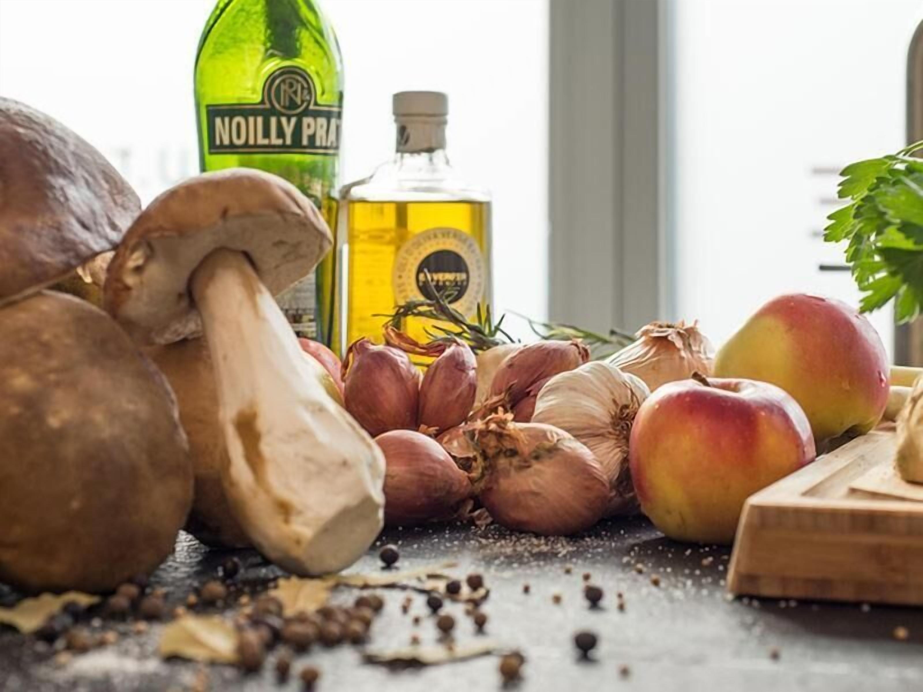 A kitchen counter with ingredients like mushrooms, garlic, and an onion, along with a bottle of oil and a cutting board.