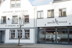 Un edificio con los letreros 'Hensens Residenz' y 'St. Jacques', y 'Die Genuss Schule' en la fachada.