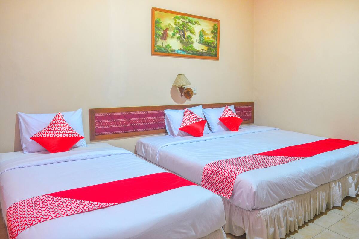 A hotel room with two beds, each with white bedding and red accents, a painting on the wall, and a bedside lamp.