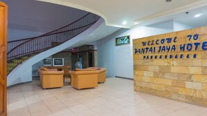 A hotel lobby with a curved staircase, a reception desk, and a sign welcoming guests to Pantai Jaya Hotel. - Hotel O Pantai Jaya (Pangandaran)
