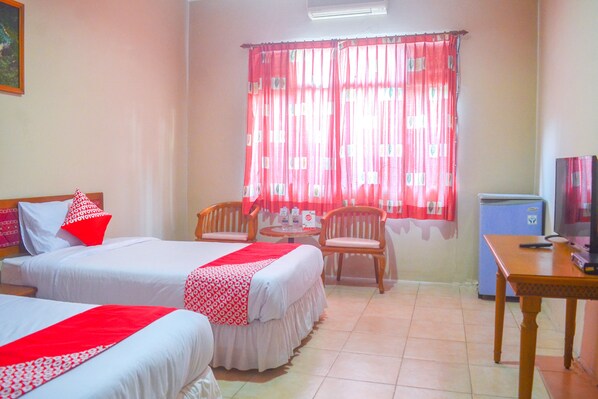 A hotel room with two beds, a small table, two chairs, a television, and a refrigerator.