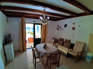 Un espace repas comprenant une table, des chaises, un canapé, un téléviseur et une vue sur l’extérieur, visible à travers une porte.