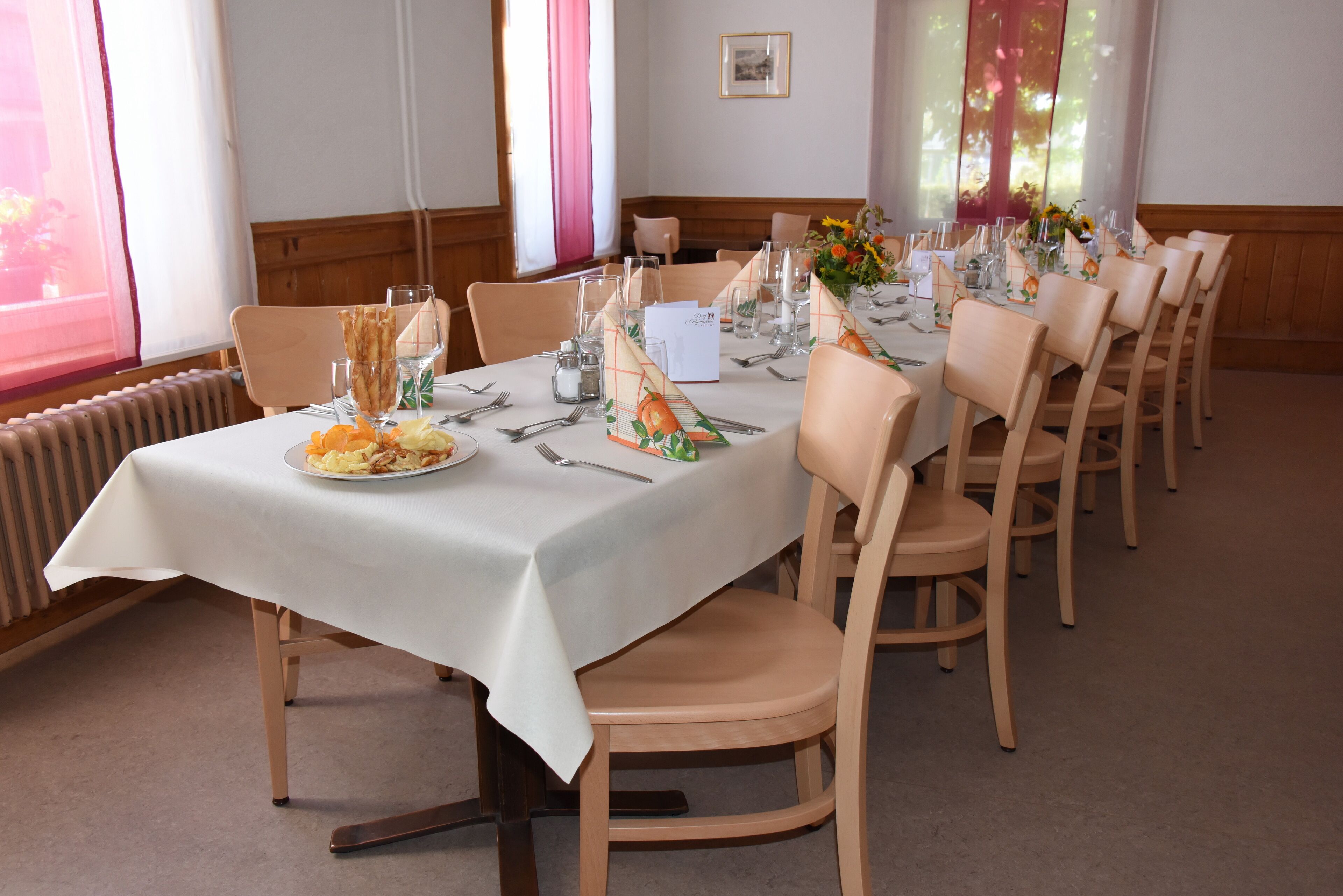 A dining area with a long table set for a meal, surrounded by chairs.