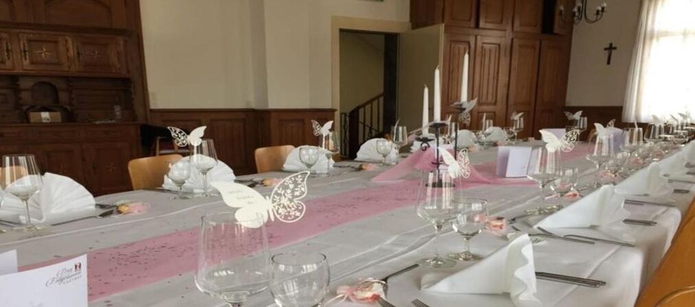 Een lange eettafel gedekt met witte tafellinnen, servies en bloemstukken.