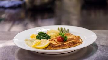 Une assiette contenant une escalope panée, des tranches de citron, des brocolis et une tomate cerise.