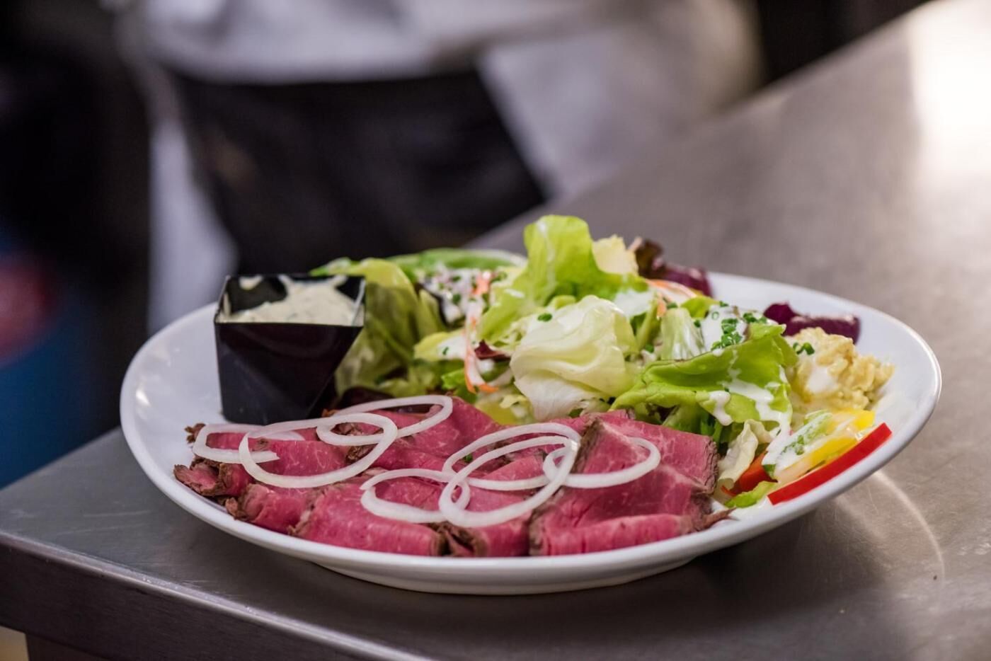 Ein Teller mit einem Steak, Salat und einer kleinen Soße.