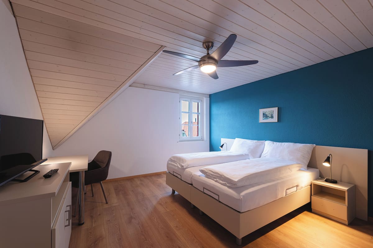 Un dormitorio con cama, escritorio, silla, ventilador de techo y mesita de noche con lámpara.