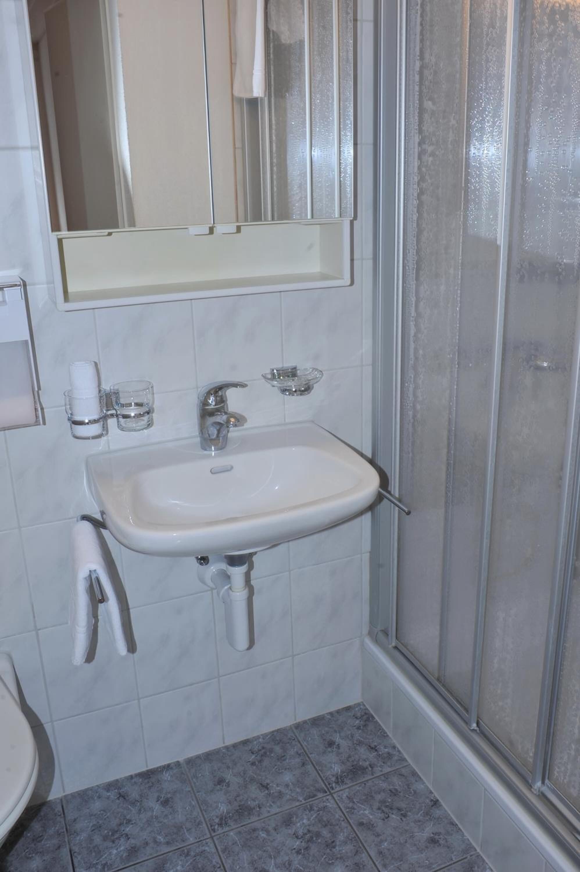 Een badkamer met een wit wastafelmeubel, spiegel en douchecabine.