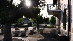 Un café en plein air avec des tables et des chaises, un arbre et un bâtiment doté d’un balcon.