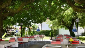 Un espace de restauration en plein air, avec des tables et des chaises, entouré d’arbres et d’une haie.