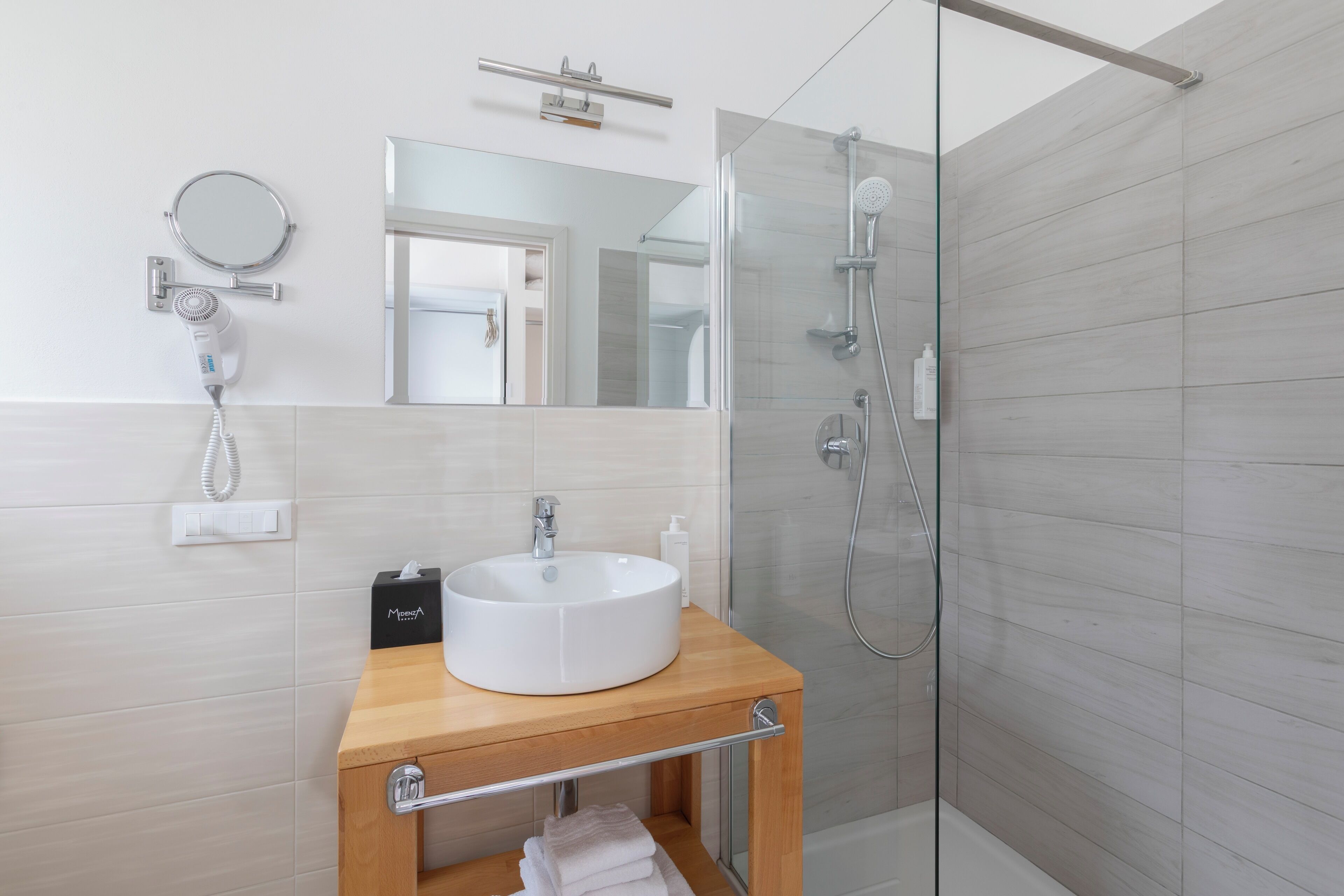 A modern bathroom with a round mirror, a white sink, and a glass-enclosed shower.