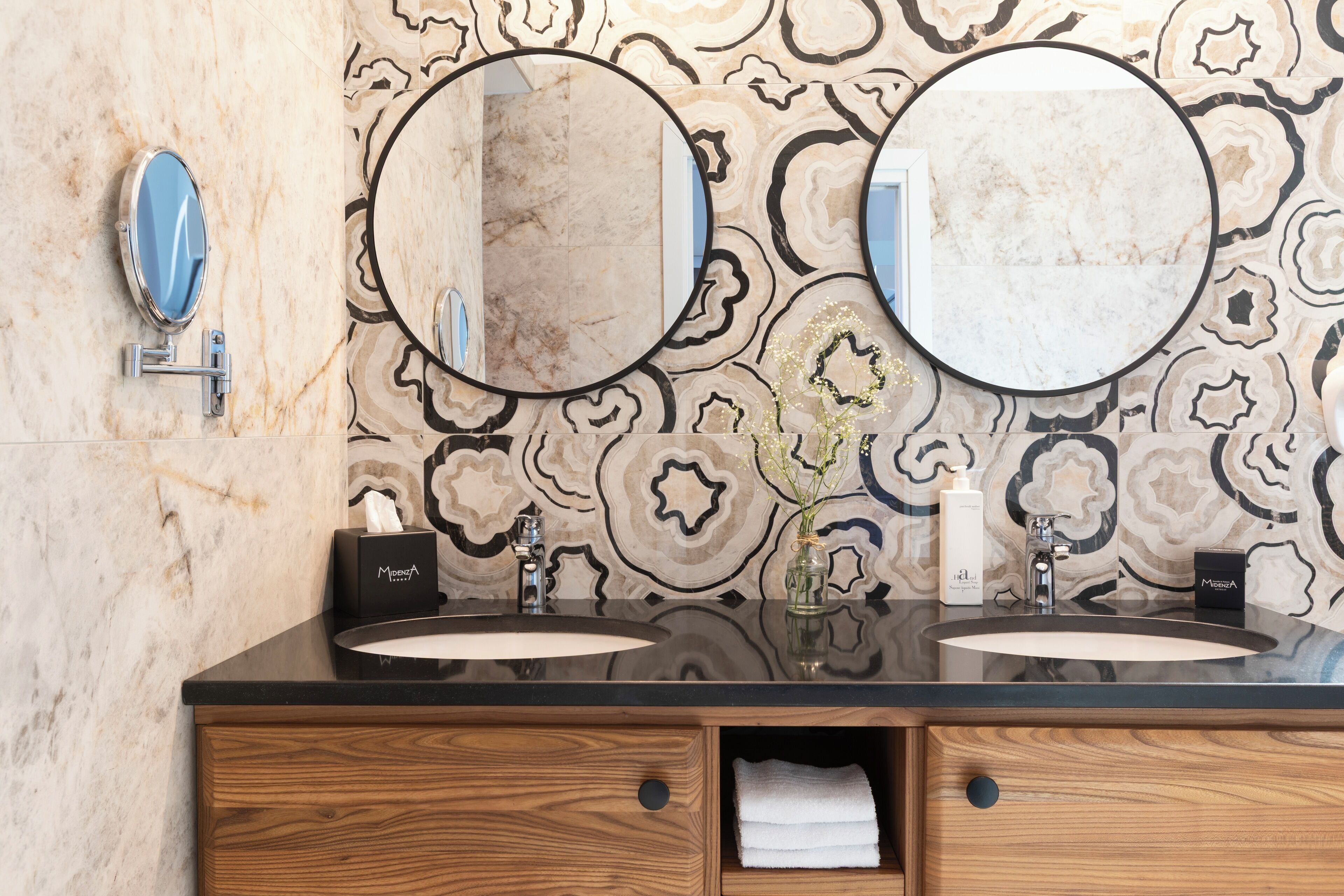 Ein Badezimmer mit zwei Waschbecken, einem Holzkosmetikschrank und dekorativen Wandfliesen.