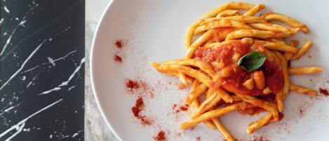 Un plato de espagueti con salsa de tomate y una hoja de albahaca como decoración, espolvoreado con condimento rojo, sobre un plato blanco.