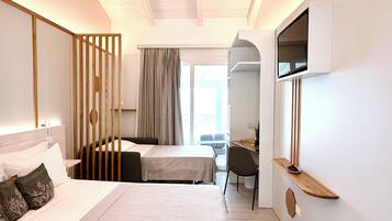 A modern hotel room with a bed, a desk, and a chair. There is a window with curtains, a mirror, and a small table with a bowl of fruit.