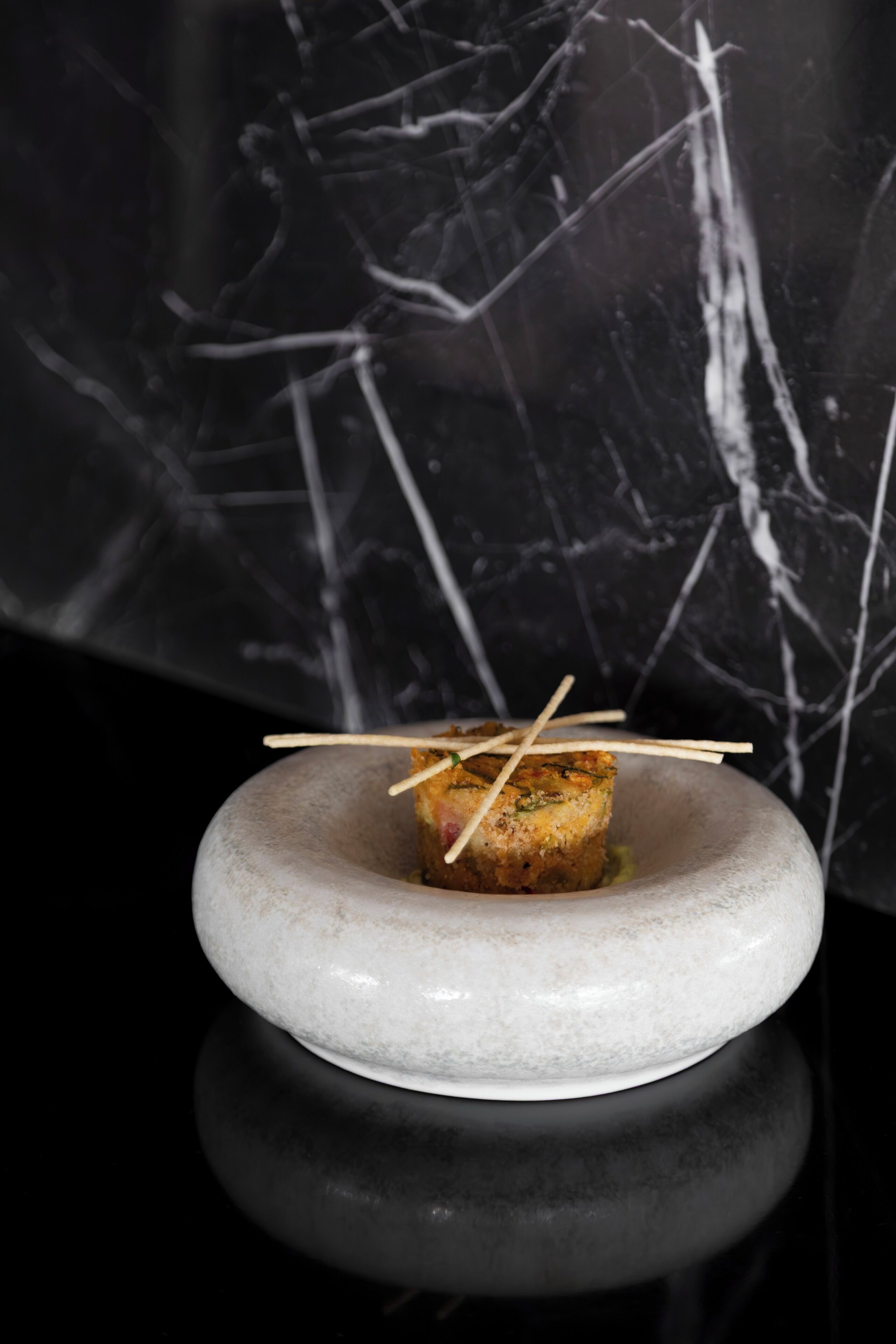 Un plat avec un cure-dent, posé sur une assiette blanche, le tout mis en valeur par un fond sombre à motifs de marbre.