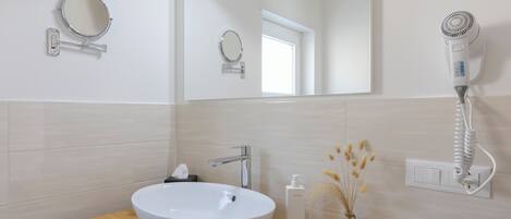 A bathroom with a white sink, a mirror, a hairdryer, and a small vase with dried flowers.