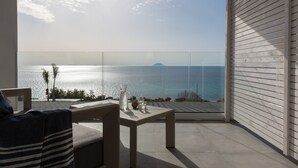 A balcony with a view of the sea, a table with glasses and a bottle, and a striped chair.