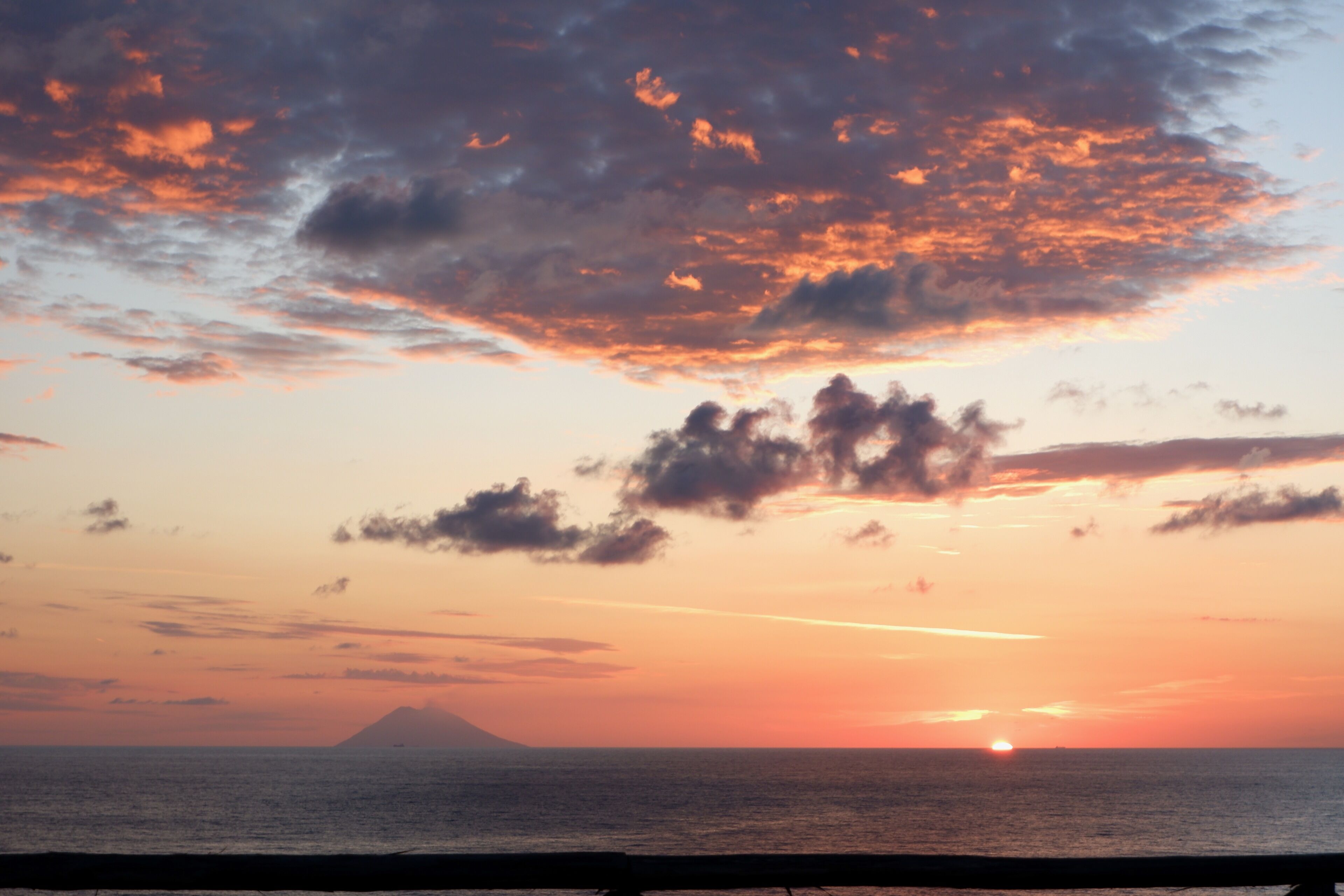 A sunset over the ocean with a mountain in the distance.
