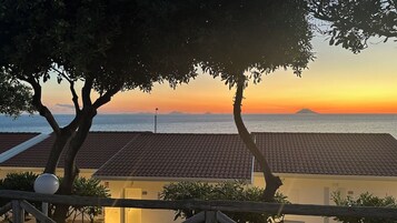 Vista costera con un atardecer, un tejado de baldosas y una bandera.