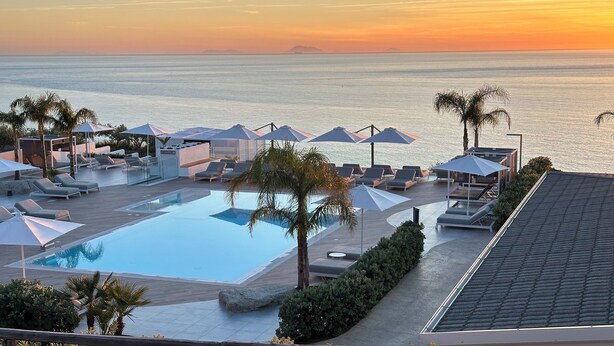A poolside area with lounge chairs and umbrellas, overlooking a body of water at sunset.