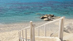 A wooden staircase leading to a sandy beach with clear turquoise water and rocks in the distance.